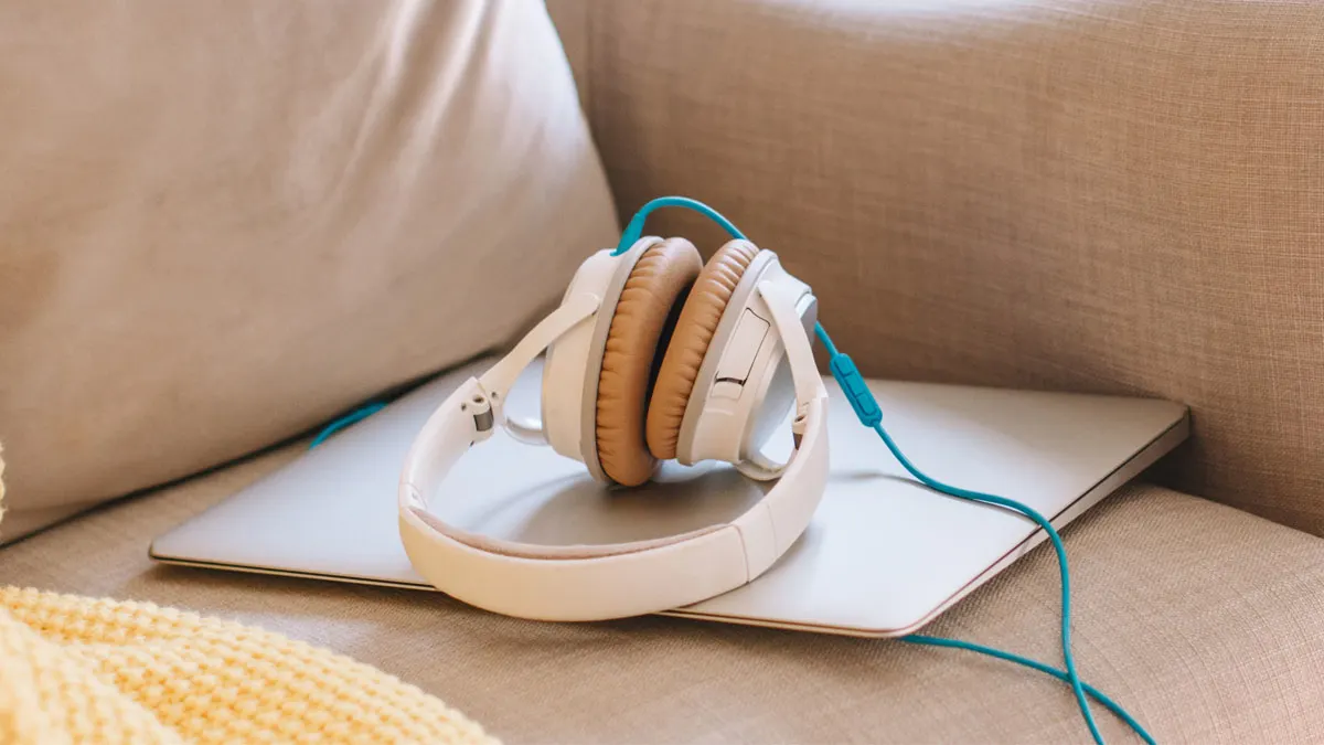 Kopfhörer liegen auf einem Laptop auf einer beigen Couch