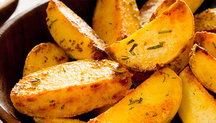 Nahaufnahme einer braunen Schüssel gefüllt mit gelben Kartoffelkeilen, die mit grünen Kräutern bestreut sind.