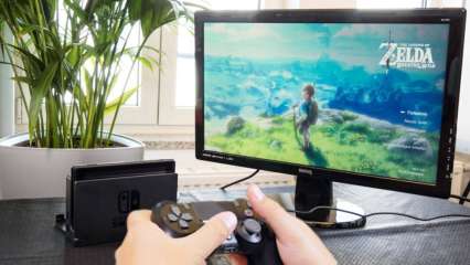 Eine Person hält einen Playstation 4 Controller in der Hand, während eine Switch und ein Monitor daneben auf dem Schreibtisch stehen.