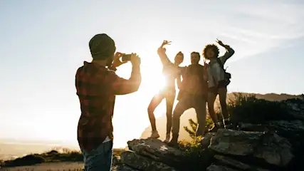 Eine Gruppe von vier Personen posiert auf Felsen, während eine weitere Person mit einem Smartphone ein Foto macht.