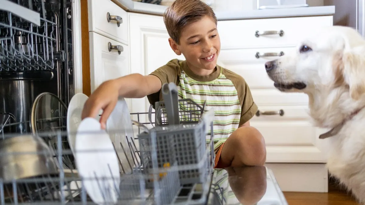 Ein Junge mit Hund nimmt Geschirr aus einem Geschirrspüler.