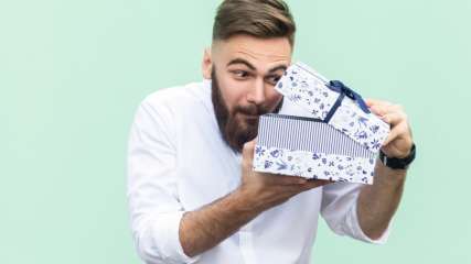 Mann mit Bart öffnet blau-weiße Geschenkbox.