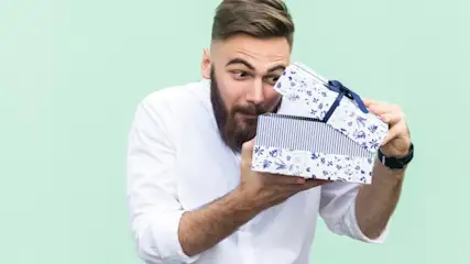 Ein Mann im weißen Hemd öffnet eine blau-weiß gestreifte Geschenkbox vor einem hellgrünen Hintergrund.