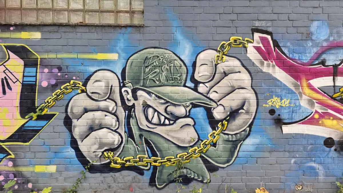 Das Foto zeigt ein Graffiti einer männlichen Person mit Baseball-Kappe, die eine goldene Kette in den Händen hält.