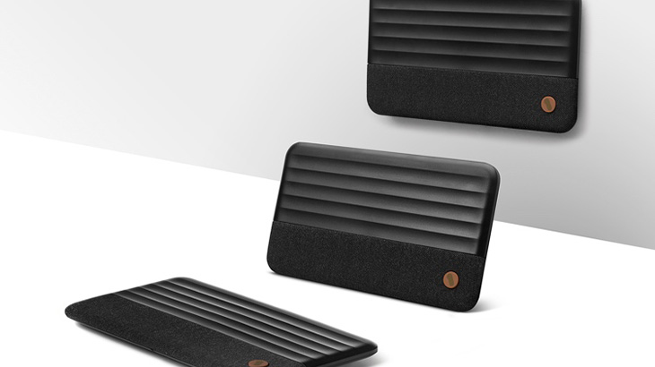 Drei schwarze, rechteckige Geräte mit horizontalen Linien und einem runden Knopf liegen auf einer weißen Oberfläche vor einer weißen Wand.