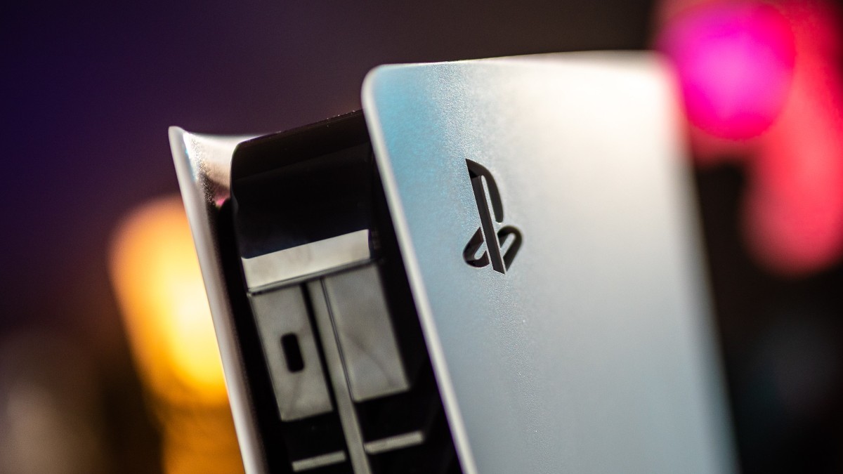 Eine PlayStation 5-Konsole steht mit sichtbarem Logo auf einer hellen Oberfläche vor einem dunklen Hintergrund mit farbigen Lichtpunkten.