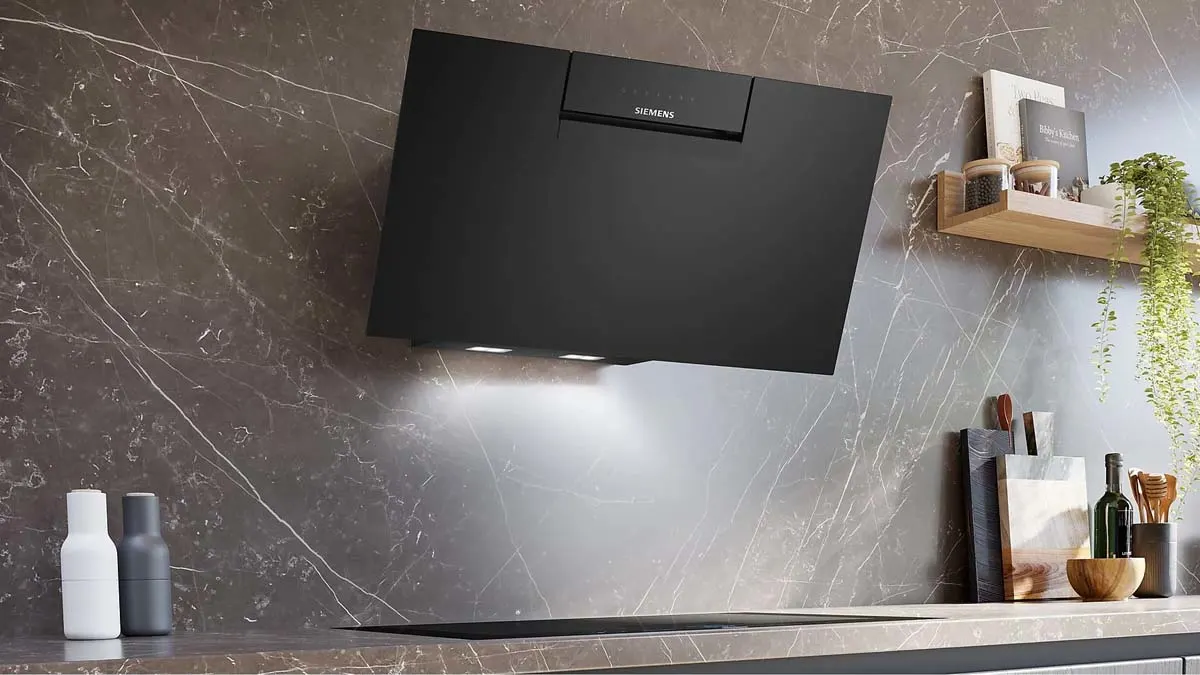 Eine schwarze Dunstabzugshaube von Siemens hängt an einer marmorierten Wand über einem Kochfeld. Auf der Arbeitsplatte stehen Flaschen und Küchenutensilien.
