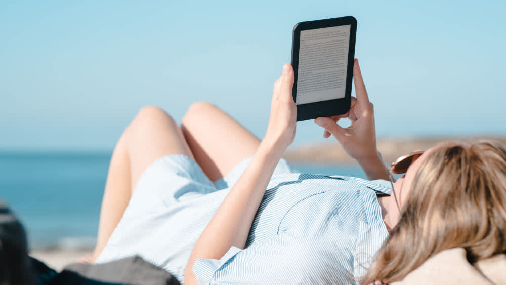 Eine Frau liegt am Strand und liest auf ihrem E-Book-Reader.
