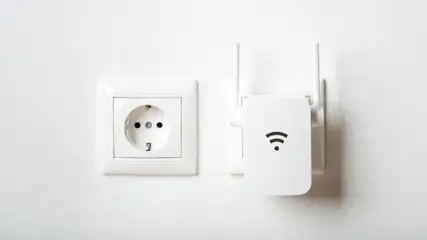 Eine weiße Steckdose ist neben einem WLAN-Verstärker mit Antennen an einer weißen Wand befestigt.