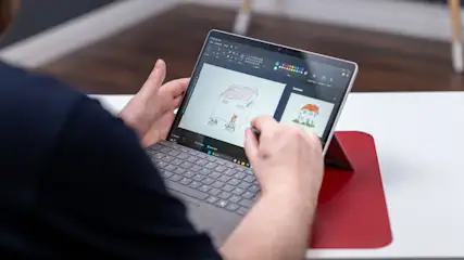 Eine Person hält ein Tablet mit Stift, auf dem eine Hauszeichnung zu sehen ist. Das Tablet steht auf einem roten Ständer.