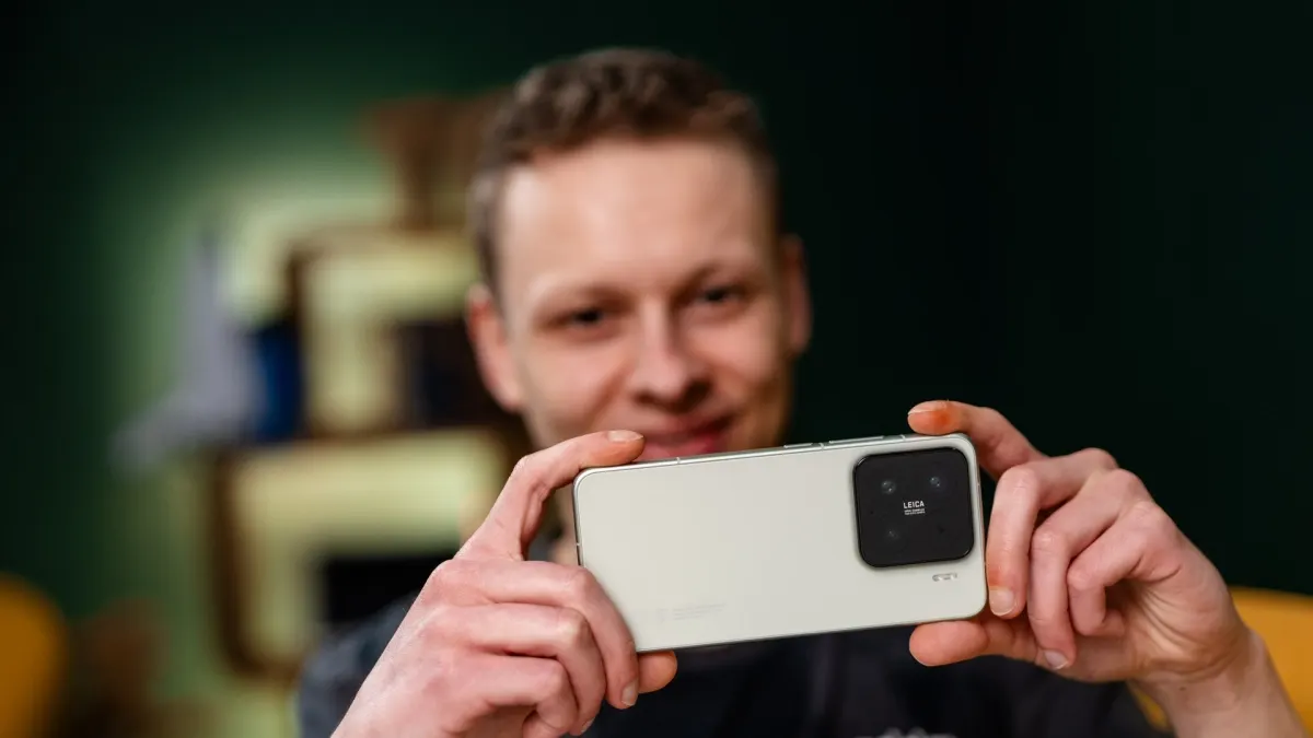 Ein Mann hält ein helles Smartphone mit einer schwarzen Kamera in horizontaler Ausrichtung vor sich. Der Hintergrund ist unscharf.