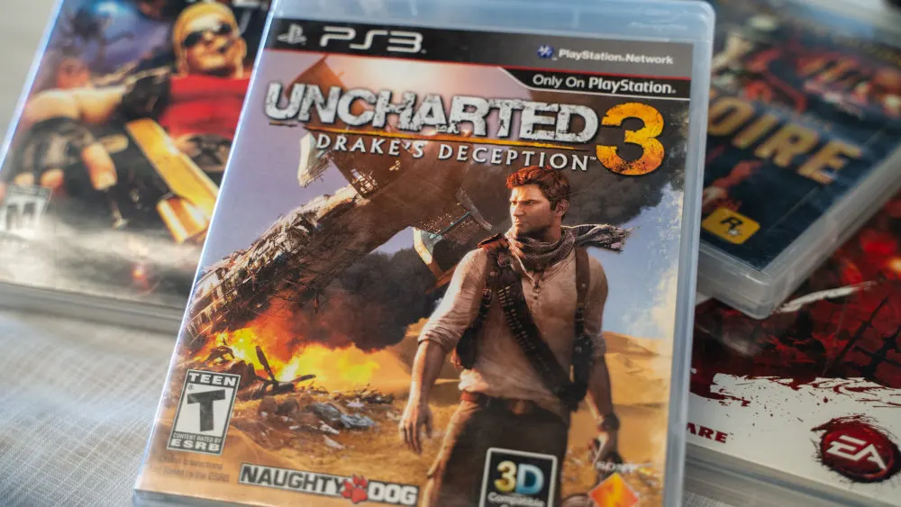 Ein Stapel von Videospielhüllen, darunter "Uncharted 3: Drake's Deception" für PS3 mit Action-Szene und "Teen"-Bewertung.