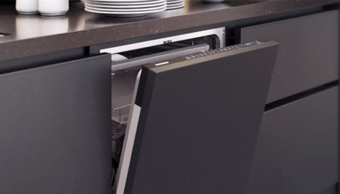 Ein Geschirrspüler mit leicht geöffneter, dunkler Tür ist unter einer dunklen Arbeitsplatte in einer Küche eingebaut. Geschirr ist oben.