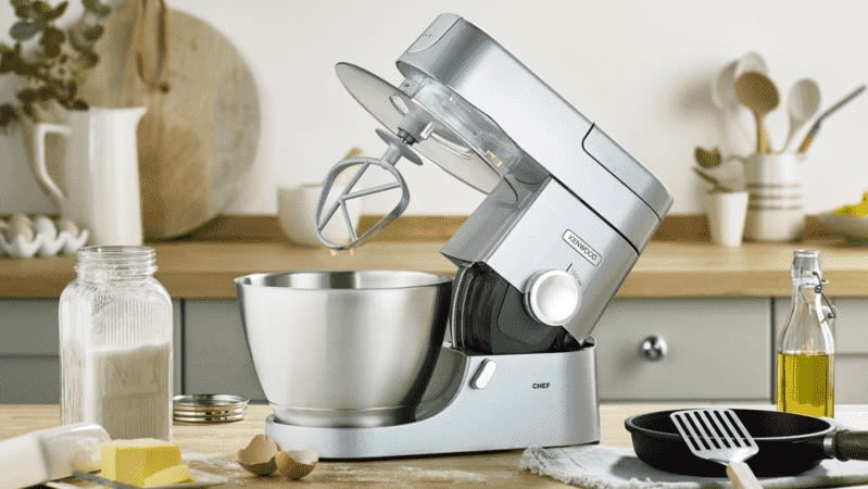 KENWOOD Chef KVC3150S Kuechenmaschine Silber (Ruehrschuesselkapazitaet: 4,6 Liter, 1000 Watt) steht in einer Kueche neben verschiedenen Backzutaten wie Mehl, Butter und Eier
