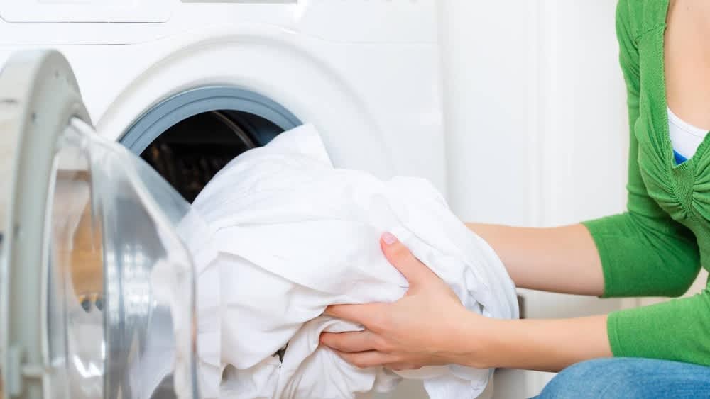 Eine Frau hält weiße Wäsche vor den Waschmaschinen Innenraum.