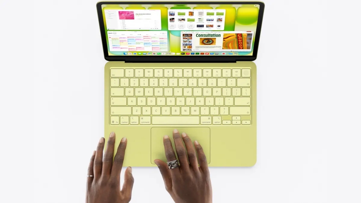 Ein gelbes MacBook Neo ist aufgeklappt von oben zu sehen. Die Hände einer Person liegen auf dem Touchpad.