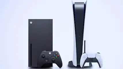 Eine schwarze Xbox-Konsole und ein Controller stehen neben einer weißen PlayStation-Konsole und einem Controller.