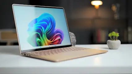 Ein Laptop mit farbigem Bildschirm steht auf einem weißen Tisch. Eine kleine Pflanze und eine Lampe sind im Hintergrund.