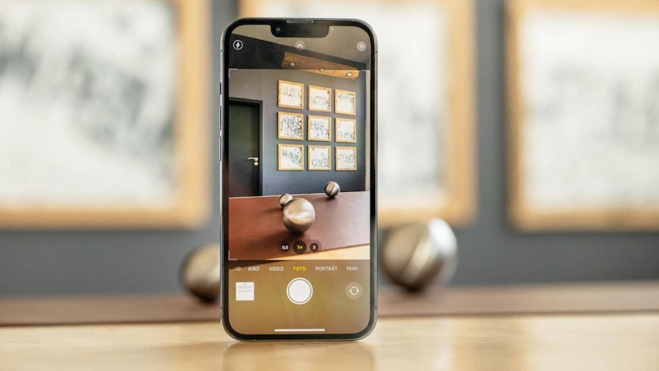 Das iPhone 13 Pro steht auf einem Tisch,die Kamera ist geöffnet und auf die Objekte vor dem iPhone 13 fokussiert