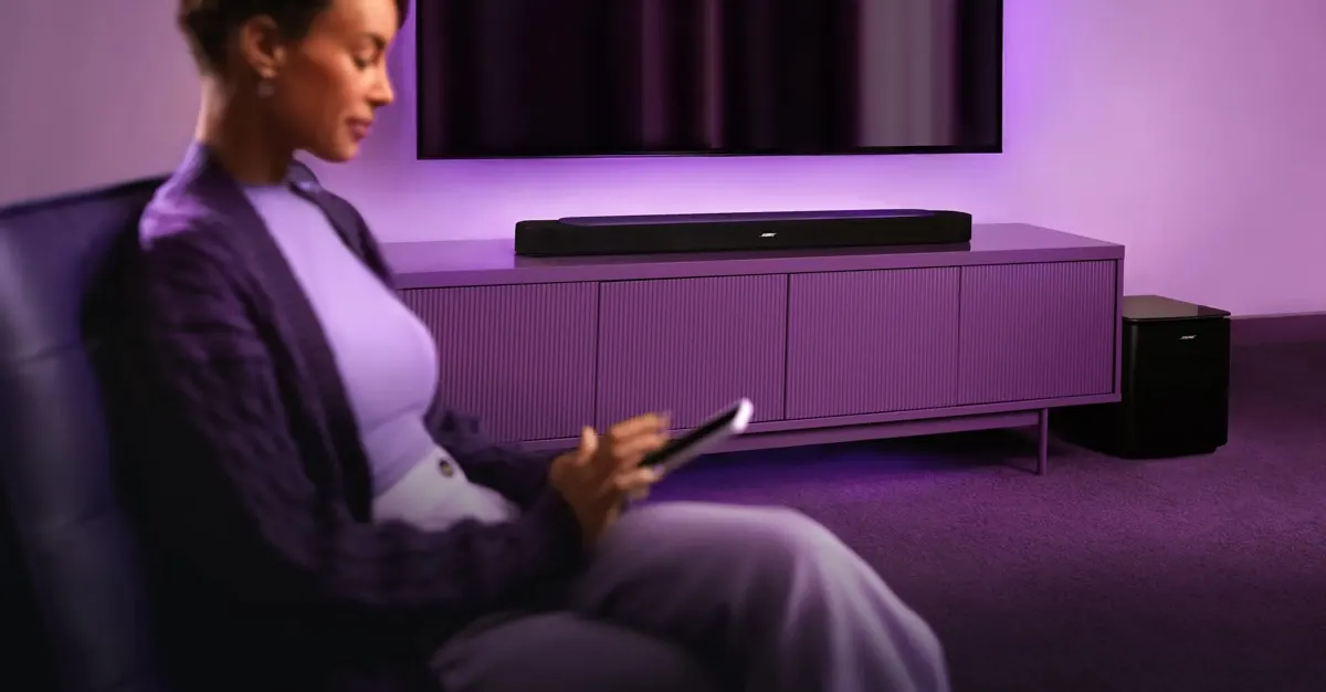 Eine Frau sitzt in einem Wohnzimmer und streamt über die Bose Lifestyle Ultra Soundbar Musik.