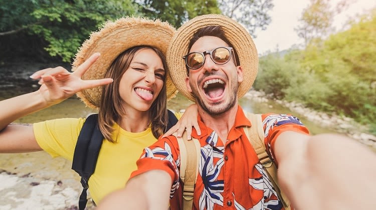 Selfie Aufnahme eines Pärchens mit Strohhueten und sommerlichen Outfits in der Natur 