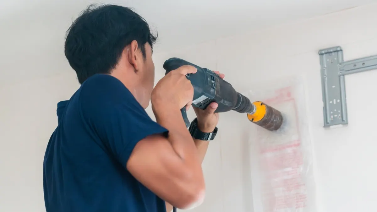 Eine Person bohrt mit einer Bohrmaschine in eine Hauswand.