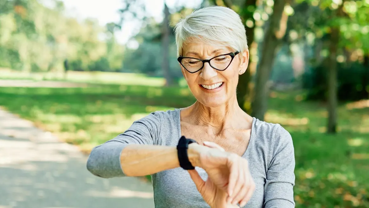 Eine ältere Frau blickt lächelnd auf ihre Smartwatch am Handgelenk.