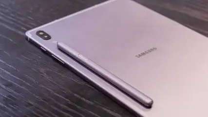 Ein lila Tablet liegt auf einer dunklen Holzoberfläche. Ein Stift liegt auf dem Tablet. Auf dem Tablet steht der Schriftzug "SAMSUNG".