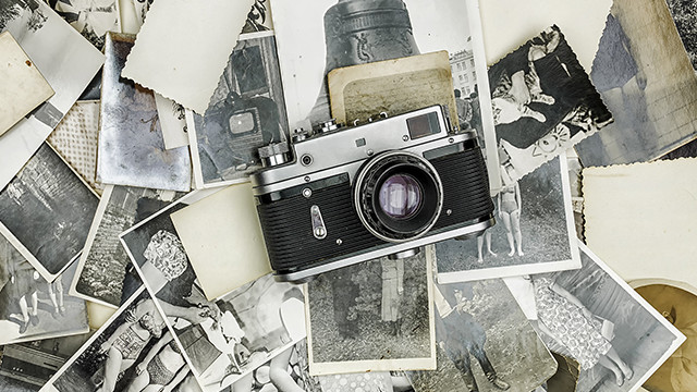 Eine silberne und schwarze Vintage-Kamera liegt auf einem Haufen alter Schwarz-Weiß-Fotografien und losen Papierstücken.