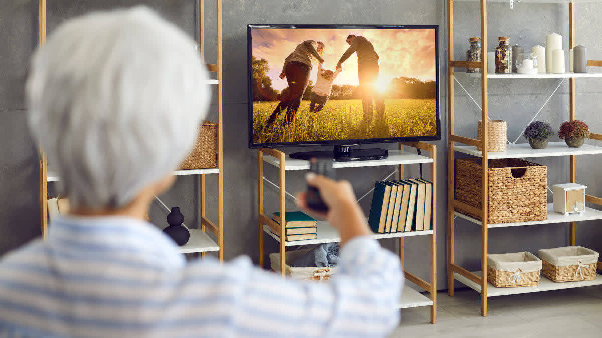 Eine Seniorin schaut sich im Wohnzimmer Fotos auf einem Fernseher an.
