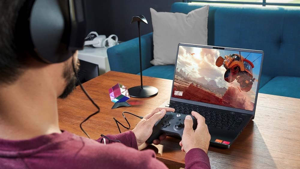 Ein Mann mit einem Xbox Controller in den Händen sitzt vor einem Schreibtisch und zockt über den Bildschirm eines Laptops.