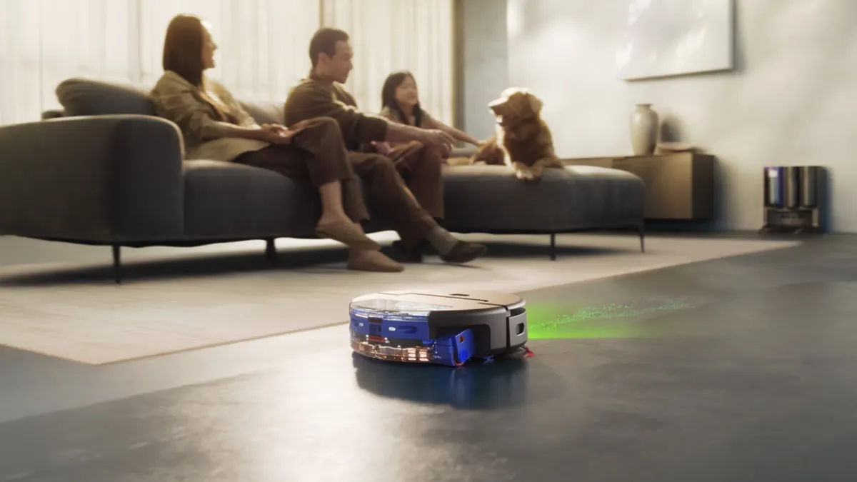 Drei Personen sitzen mit einem Hund auf einer Couch, während der Dyson Spot+Scrub Ai den Boden saugt und wischt.