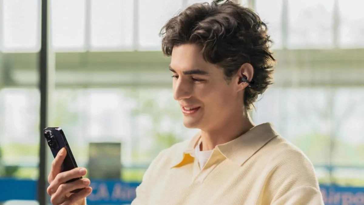 Ein Mann trägt die Open-Ear-Kopfhörer Shokz OpenDots 2 und blickt auf sein Smartphone.