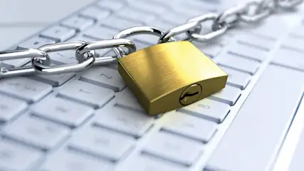 Ein goldenes Vorhängeschloss sichert eine silberne Kette auf einer weißen Computertastatur.
