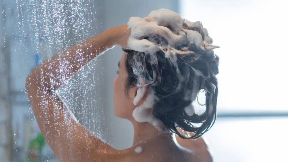 Eine Frau in der Dusche massiert sich Shampoo in die Haare
