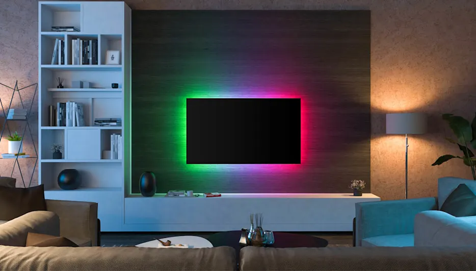 Ein Wohnzimmer mit Sofa, Tisch und Fernseher mit stimmungsvoller RGB Beleuchtung hinter dem TV und Lampen mit warmen Licht.