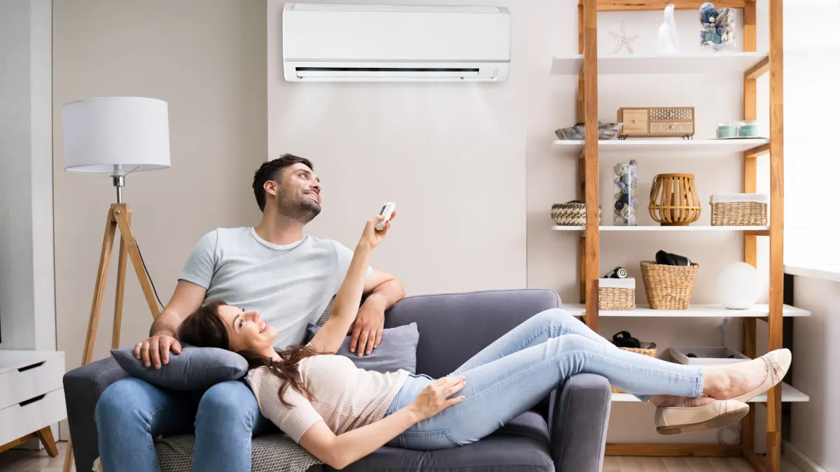 Eine Frau liegt im Wohnzimmer mit ihrem Kopf auf dem Schoß eines Mannes und bedient mit einer Fernbedienung eine Split-Klimaanlage.