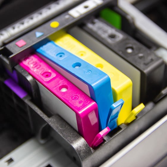 Vier Druckerpatronen in den Farben pink, blau, gelb und schwarz sind in einem Drucker.