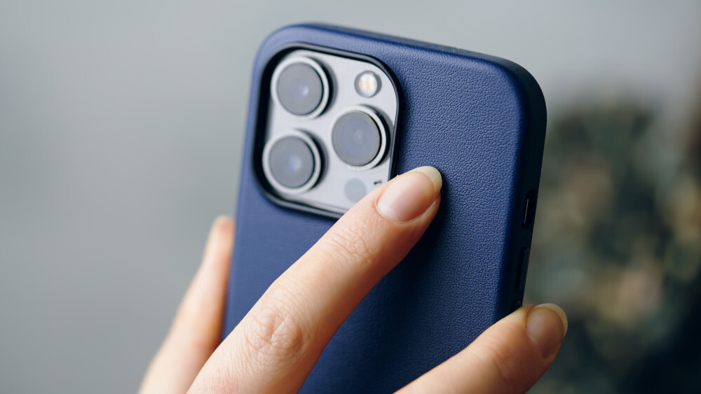 Nahaufnahme eines blauen Telefons mit drei Kameralinsen und einem Blitzgerät, das von einer Hand gehalten wird.