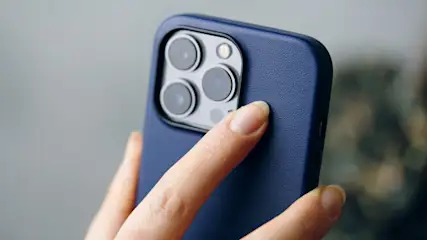 Nahaufnahme eines blauen Telefons mit drei Kameralinsen und einem Blitzgerät, das von einer Hand gehalten wird.