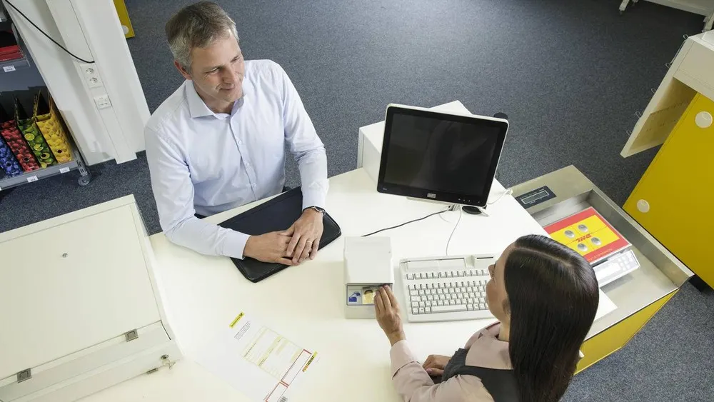 Ein Mann und eine Frau sitzen an einem Schreibtisch mit einem Computer und Dokumenten.