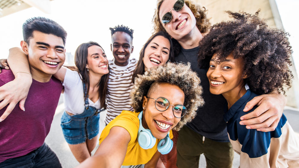 Eine Gruppe von sieben lächelnden Personen posiert für ein Foto im Freien. Sie tragen verschiedene Kleidungsstile und Accessoires.