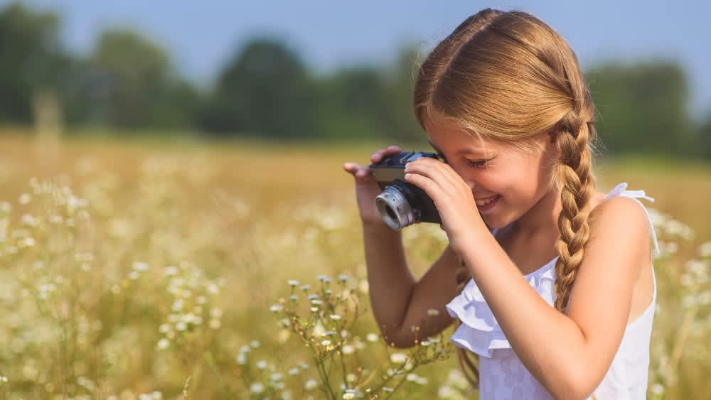 Ein Mädchen macht ein Foto mit einer Kamera auf einer Wiese.