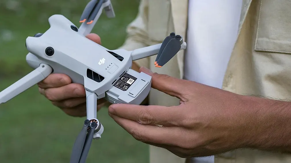 Mann hat DJI Mini 4 Pro Fly More Combo Mini-Kameradrohne in Händen und wechselt Akku mit Speicher