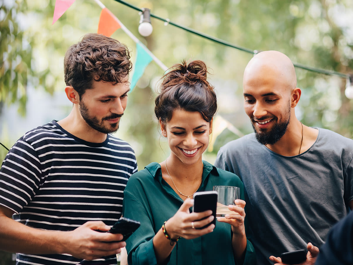 Drei Menschen im Garten mit Smartphone in der Hand betrachten ein Display und freuen sich