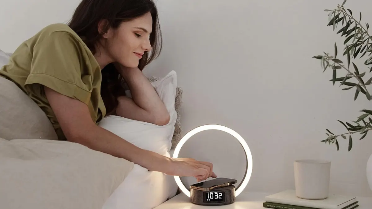 Eine Frau bedient ihr Smartphone, das auf dem Lichtwecker Beurer WL 65 liegt.