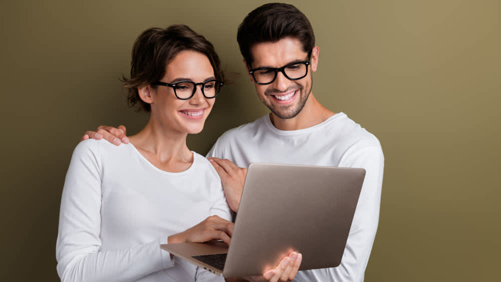 Ein Mann und eine Frau schauen glücklich auf das Display eines Notebooks.
