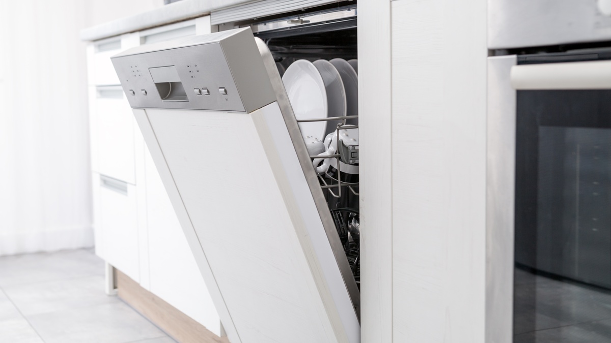 Geöffneter, weißer Geschirrspüler mit silberner Blende in einer weißen Küche. Geschirr und Tassen sind im Inneren sichtbar.