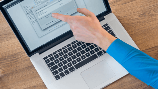 Eine Person mit blauem Hemd bedient einen Laptop mit einer geöffneten Dialogbox auf einem Holztisch.