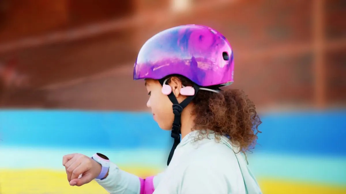 Mädchen mit lila Helm und Smartwatch. Hintergrund ist blau, gelb und braun.